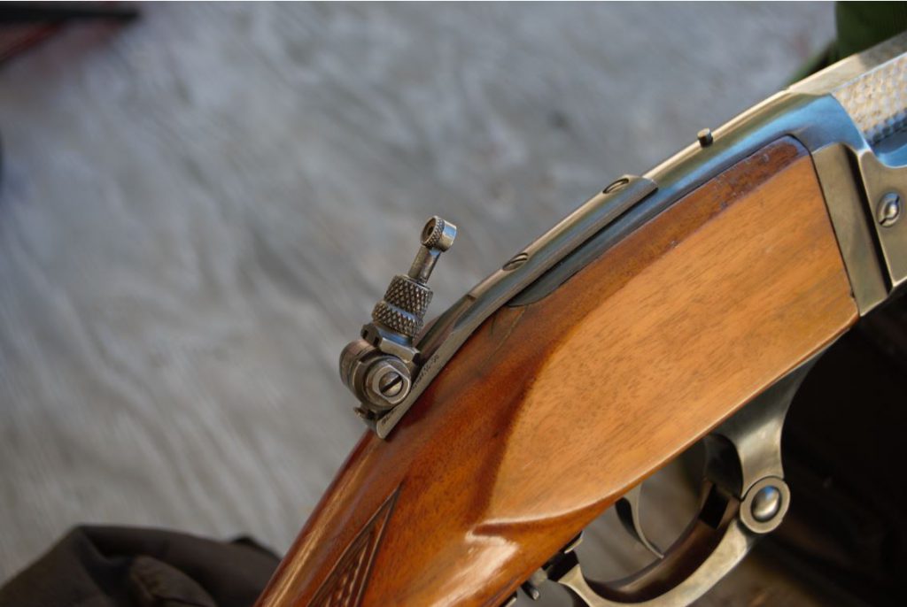 For folks (like me) who are fascinated by such things, older rifles commonly carry features not seen today. This is my Savage 1899 “.250-3000 Rifle,”, built in the late ‘teens and offered only with this incredibly cool flip-up tang-mounted aperture sight.
